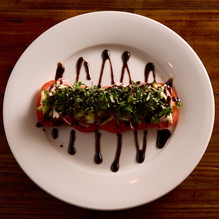 Caprese plate of sliced tomato and fresh mozzarella with balsamic glaze and micro greens