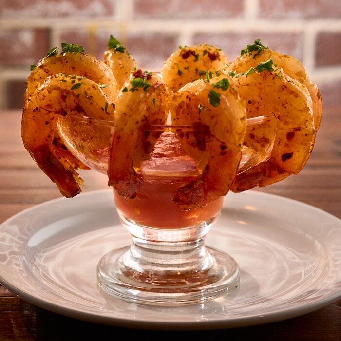 Cajun garlic tiger shrimp arranged around a glass of cocktail sauce