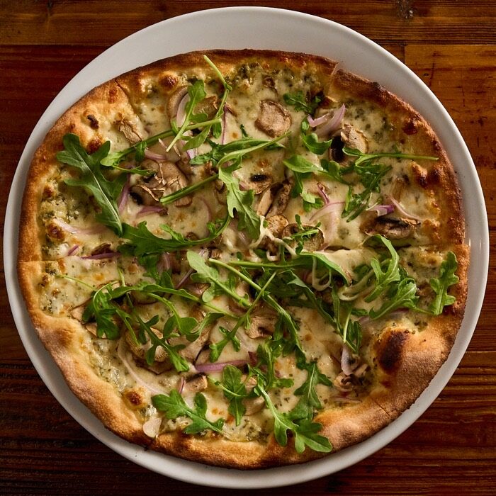 Truffle mushroom pizza with arugula, red onion and white truffle oil on alfredo pesto