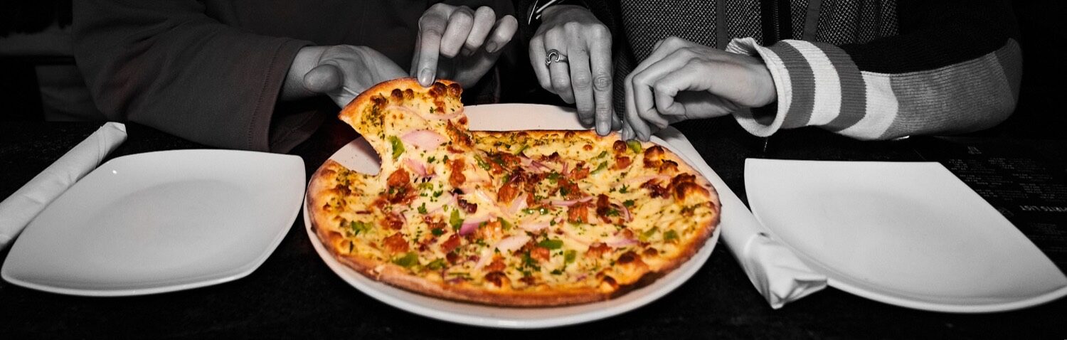 Stylized shot of a pizza on the table between two diners at JZ's Pizza