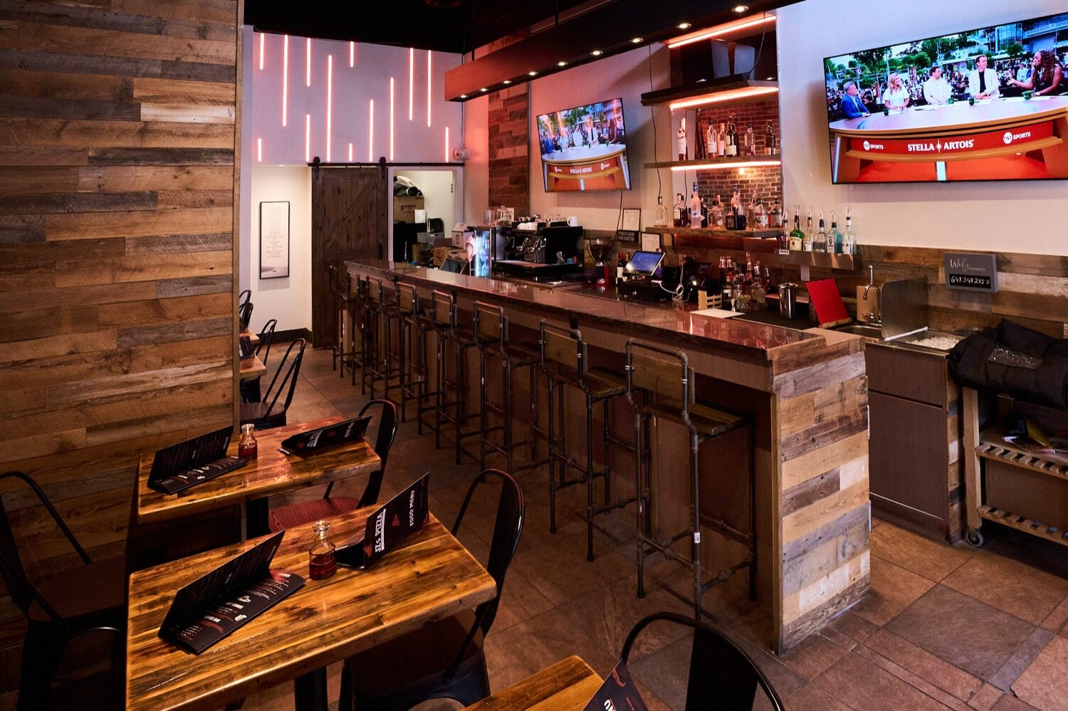 The bar at JZ's Pizza Kitchen & Sports Bar, with reclaimed wood, stools and TVs showing the game