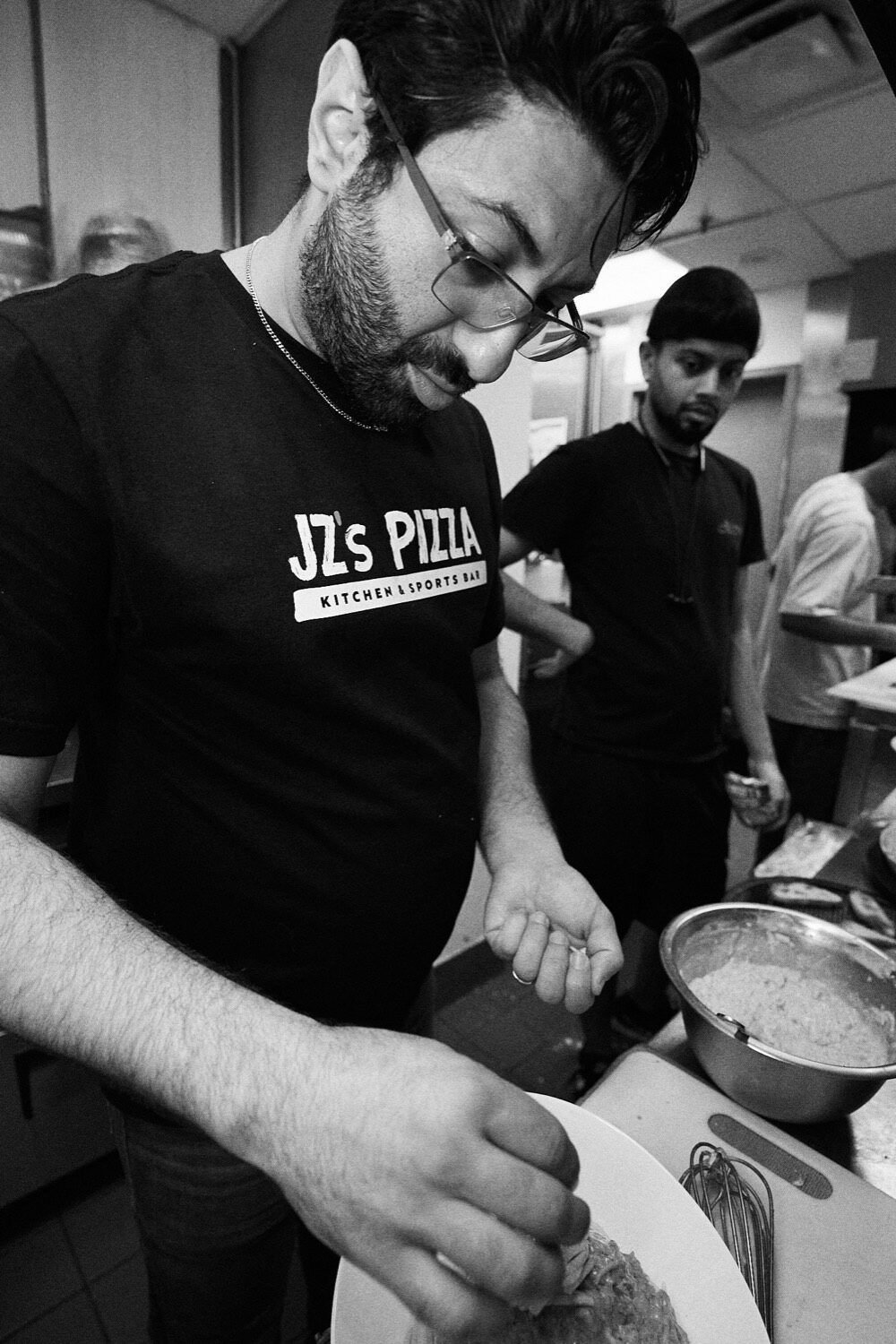 A JZ's Pizza owner plating a dish in the kitchen, in black and white