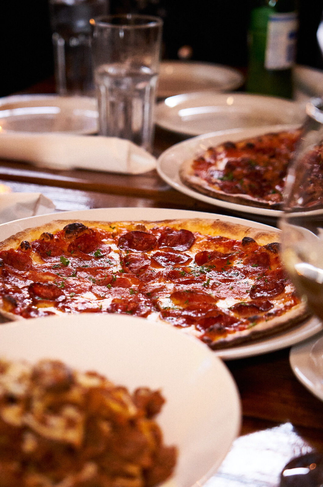 Pepperoni pizza on a shared table with pasta and drinks at JZ's Pizza