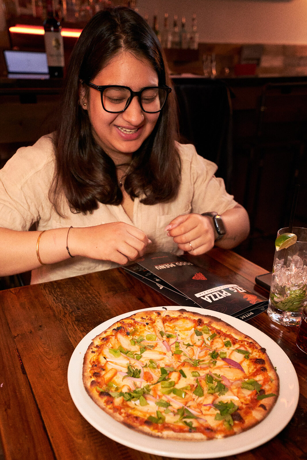Smiling guest at JZ's Pizza with a fresh pizza in front of her